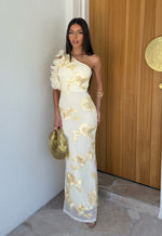 Woman in a lemon floral one-shoulder dress standing in front of a wooden door.